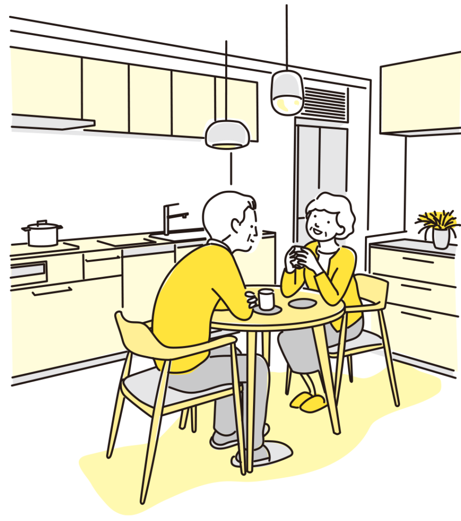 Two people sit at a round kitchen table, chatting and drinking coffee in a bright, modern kitchen with yellow accents.