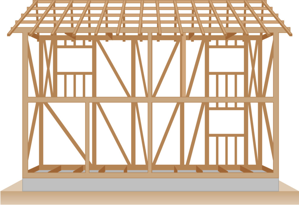 Timber-framed two-story house under construction with roof trusses and wall studs on a concrete foundation.